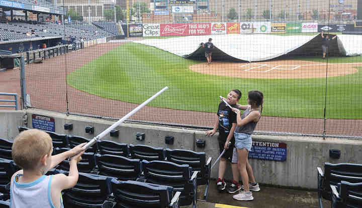 Addie Medina (right) gains the upper hand against her twin brother Easton Medina in a lightsaber duel as Keegan Martin (far left)  looks to make the save during Star Wars night at Fifth Third Field in Toledo.   (Jeremy Wadsworth / The Blade)